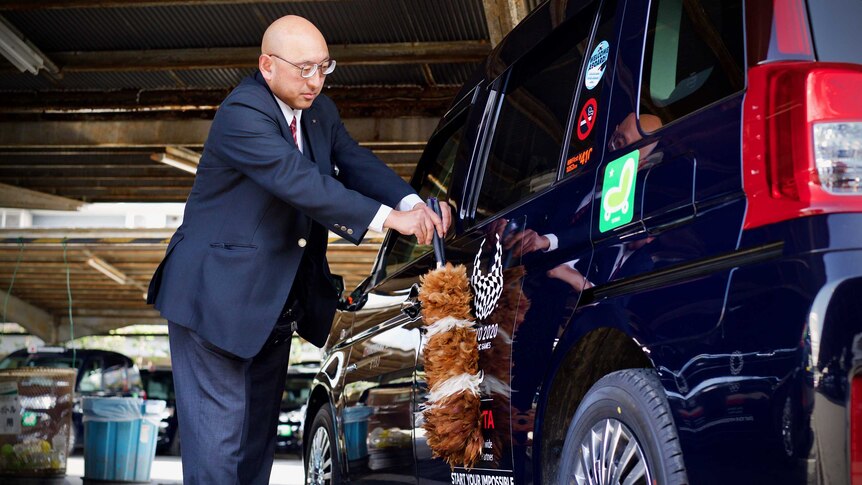 A Japanese driver cleans his taxi with a feather duster