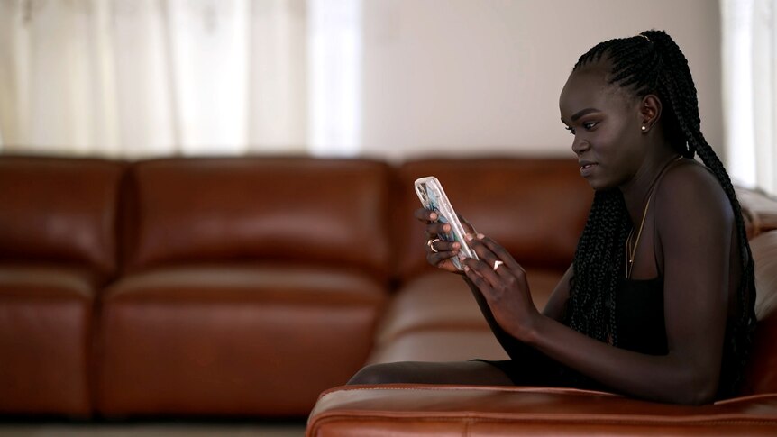Unice Wani looks at her phone as she sits on a couch.