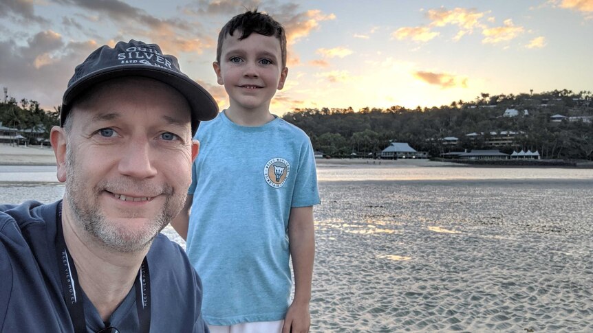 A smiling man in a cap and his son on the beach at sunset.