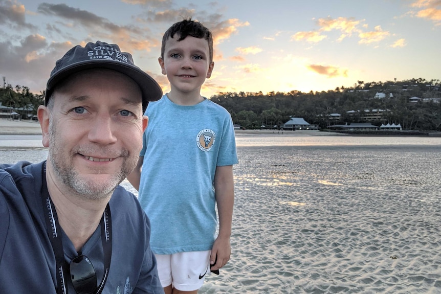 A smiling man in a cap and his son on the beach at sunset.