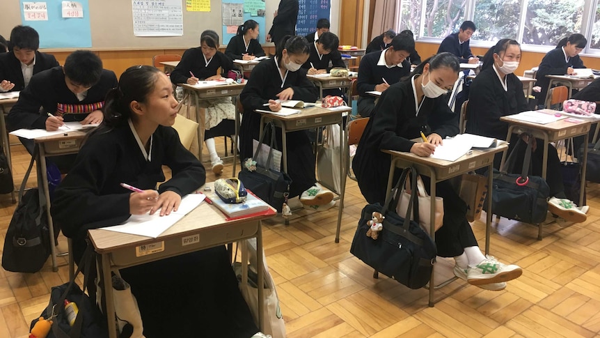A group of students write in notebooks and sit at single desks in a classroom at their North Korean school in Japan.