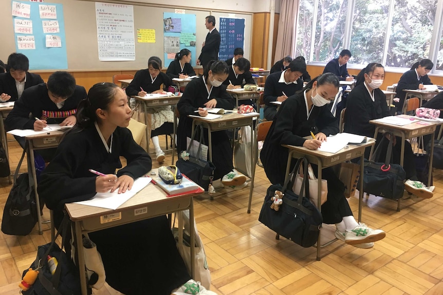 A group of students write in notebooks and sit at single desks in a classroom at their North Korean school in Japan.