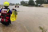 Three people wearing wet suits and helmets wade through waist deep floodwaters.