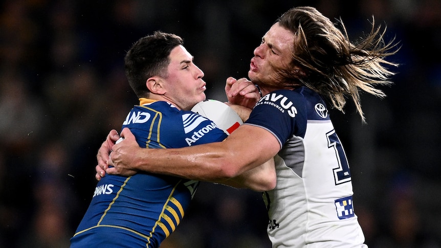 A Parramatta Eels NRL player holds the ball while being tackled by a North Queensland opponent.