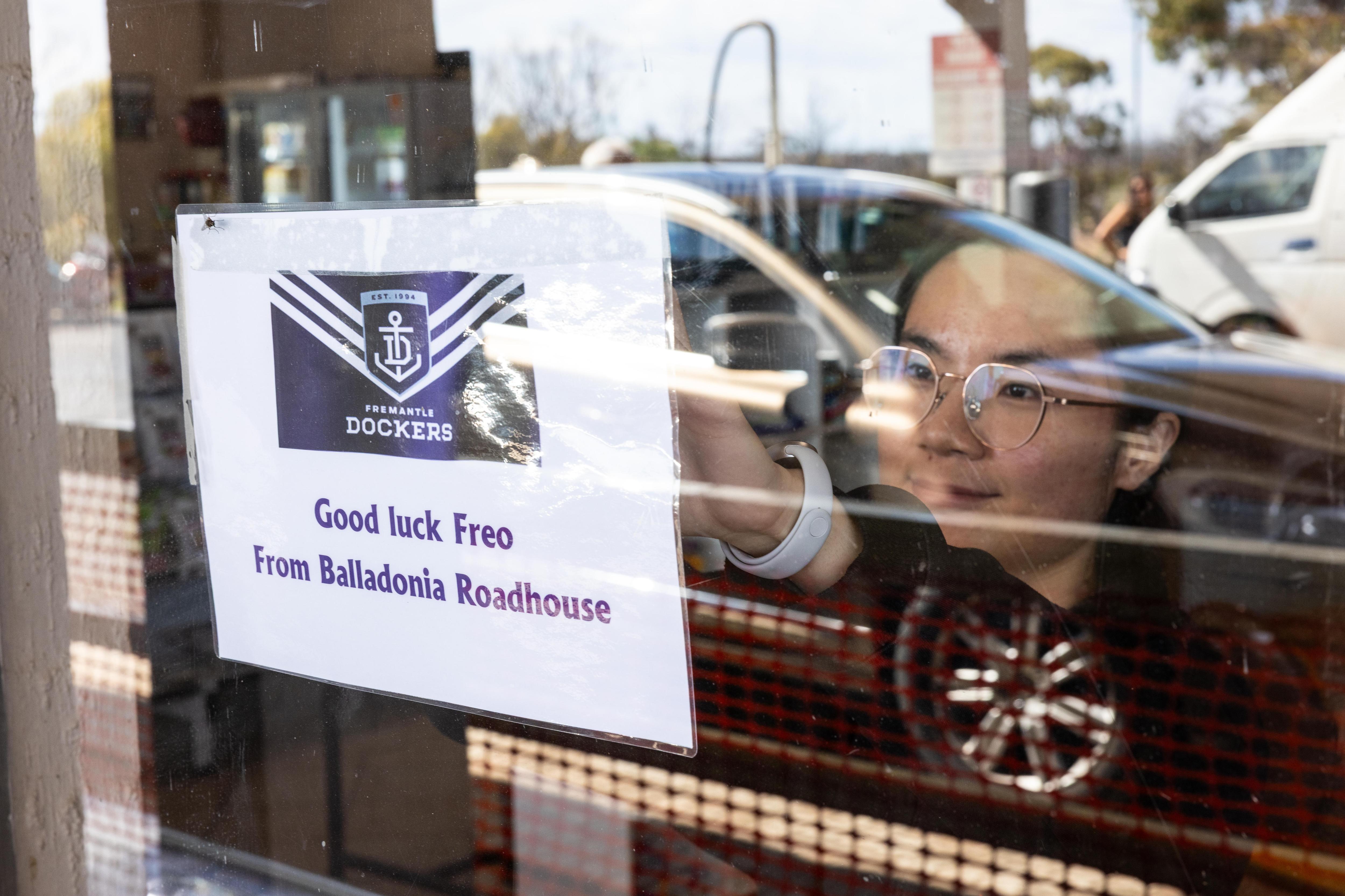 A worker pinning up a sign welcoming Fremantle Dockers fans.