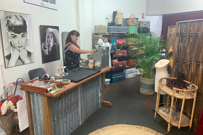 Show owner Jenny Turner behind the counter and old cash register surrounded by stacked vintage suitcases and photos of stars