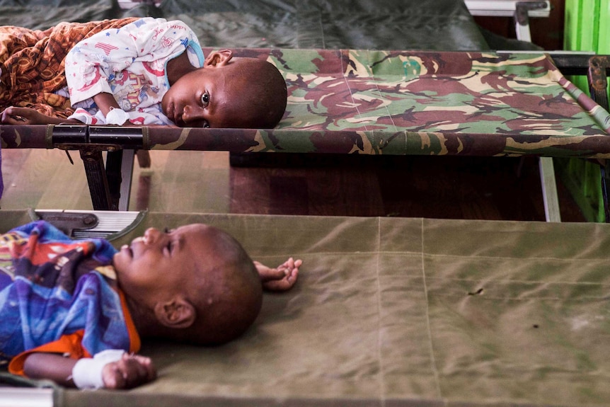 Two sick children look sad while lying on stretchers in hospital.