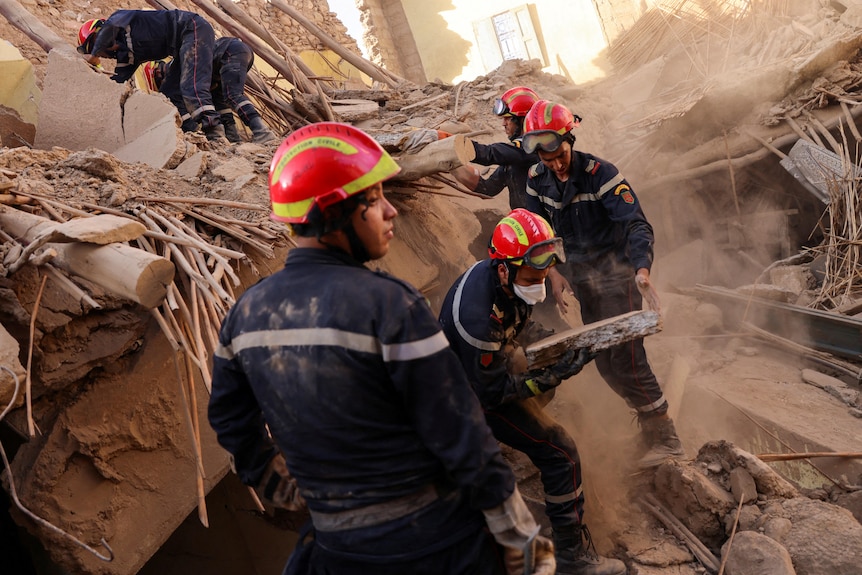 Emergency personel in red hats work their way through debris of buildings. 