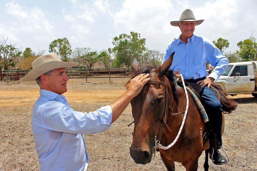 Federal member for Kennedy, Bob Katter, sits on a horse while his son Robbie, the State Member for Traeger pats the horse's face