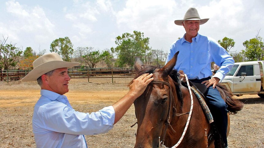 Federal member for Kennedy, Bob Katter, sits on a horse while his son Robbie, the State Member for Traeger pats the horse's face