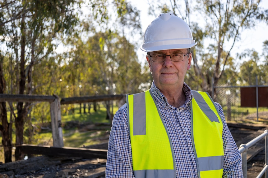 A man with a hard hat and high visibility vest stands in front of gum trees
