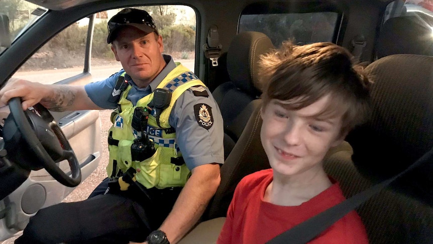 Senior Constable Smith in a police car with the boy in the front seat with him. Both are smiling.