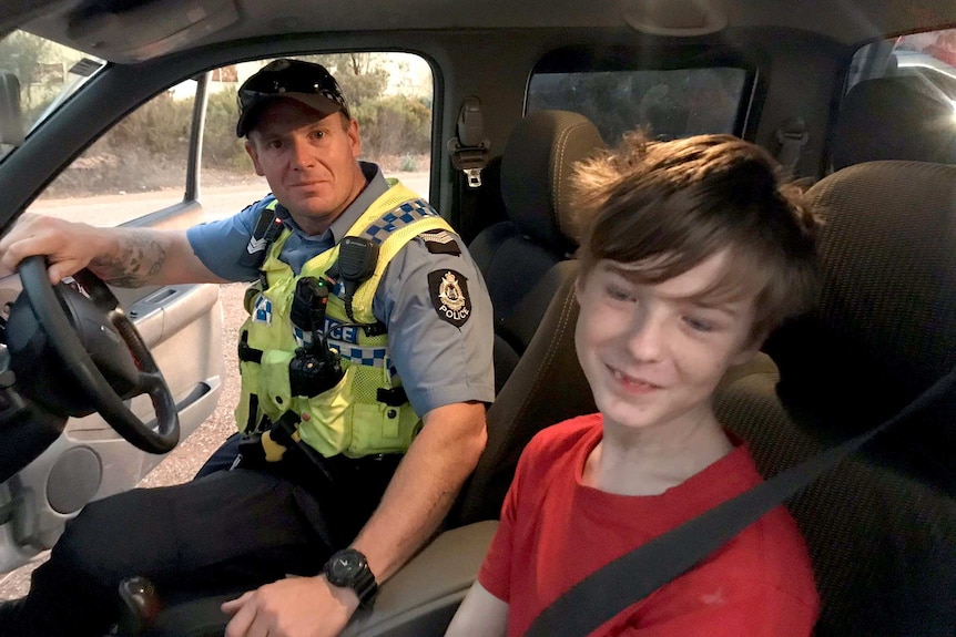 Senior Constable Smith in a police car with the boy in the front seat with him. Both are smiling.