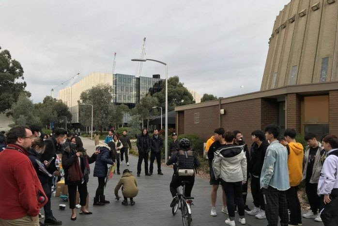 A group of Chinese and Hong Kong students stand on the footpath next to Monash University campus.