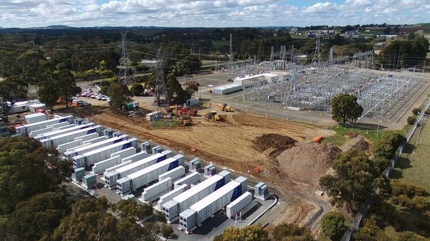 a row of shipping container looking batteries next to an electricity sub station