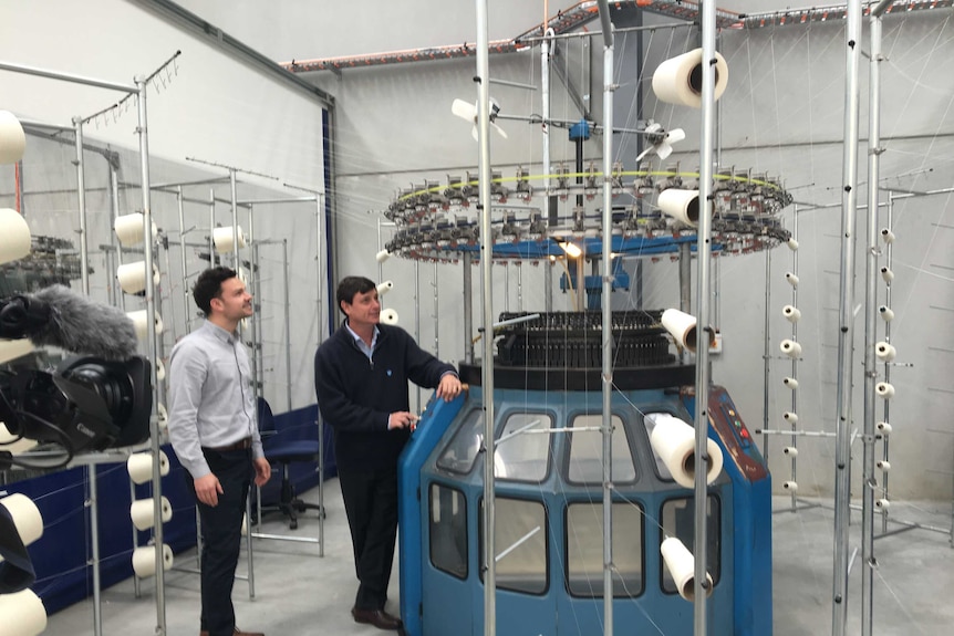 Two men stand next to a wool producing machine