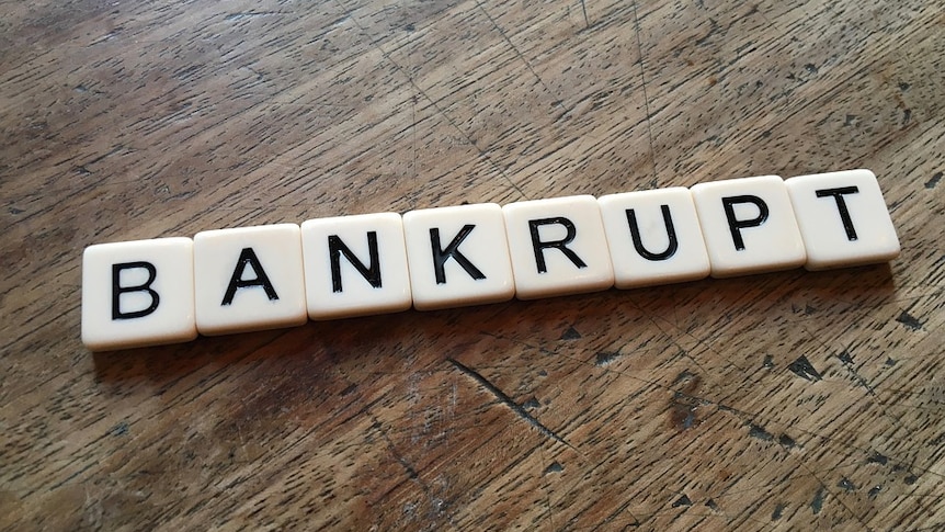 Scrabble letters lie on a wooden table spelling the word 'bankrupt'.