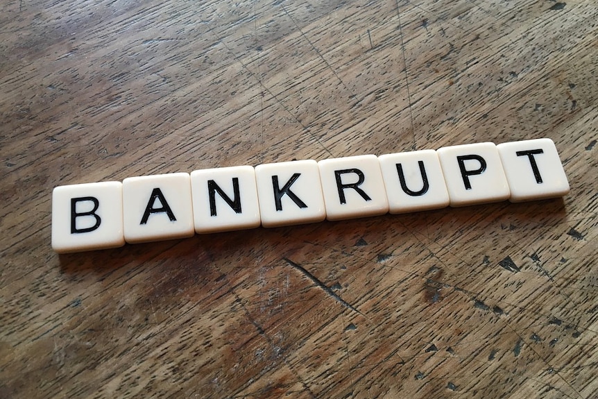 Scrabble letters lie on a wooden table spelling the word 'bankrupt'.