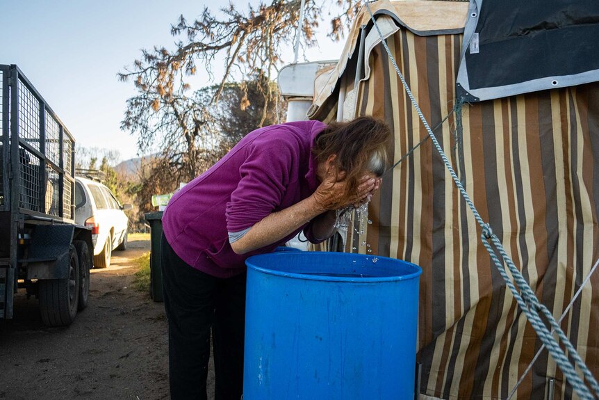Ronnie Eagles washing her face in a grain drum outside her caravan.
