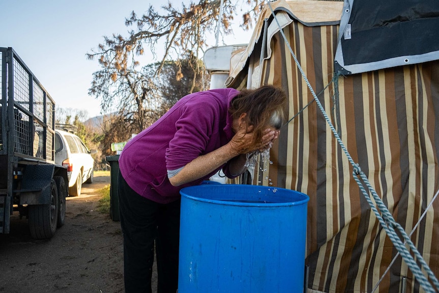 Ronnie Eagles washing her face in a grain drum outside her caravan.