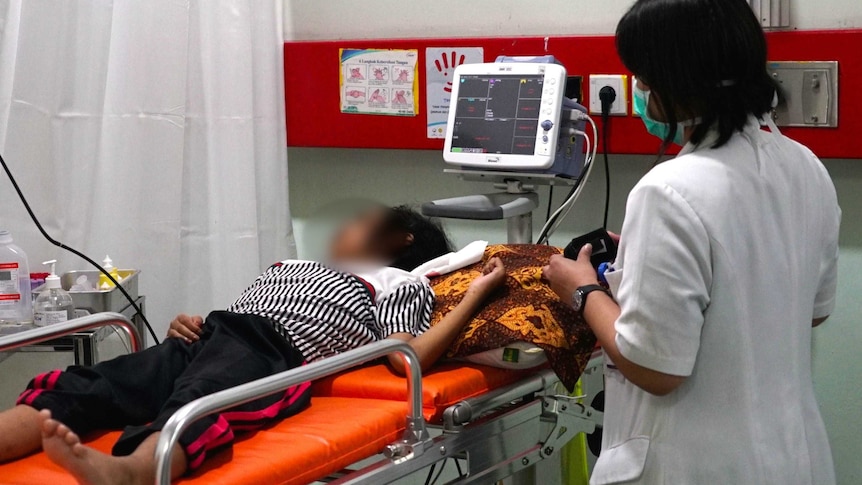 A nurse looks at a young leukemia patient lying on a bed in Jakarta's Cipto Mangunkusumo hospital.