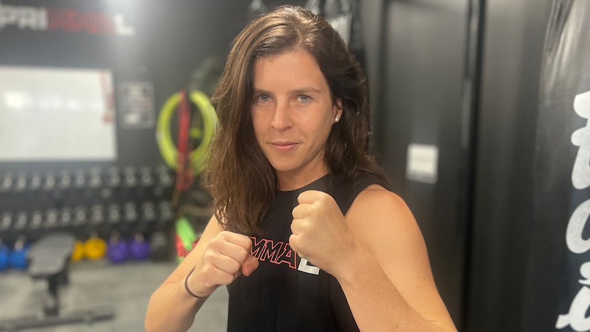 A woman in a fighting stance with her fists in front of her inside a gym.