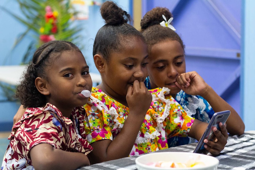 Three girls looking at their mobile phones at a community celebration.