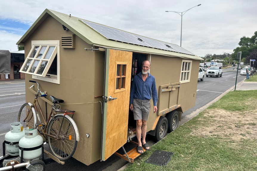 A man stands in the doorway of a tiny home on a trailer