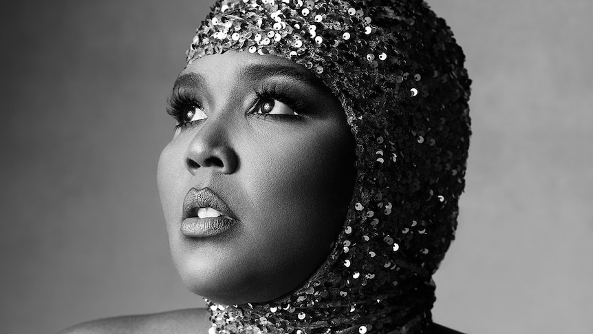Lizzo stares into the distance, wear a sparkly, sequined headdress