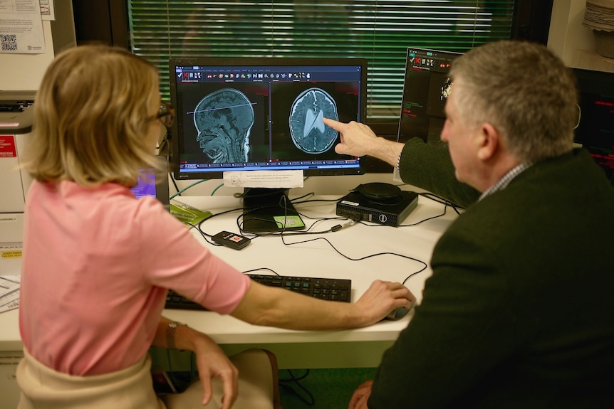 a man and woman sitting in front of computers displaying a child's brain scan