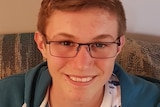 A teenage boy wearing glasses smiles at the camera.