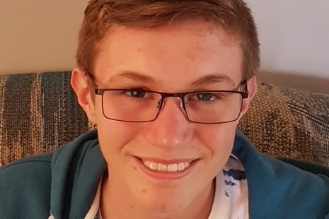 A teenage boy wearing glasses smiles at the camera.