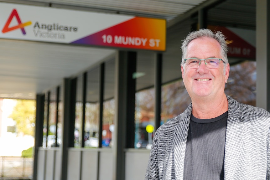 A man with glasses stands in front of an Anglicare Victoria sign.