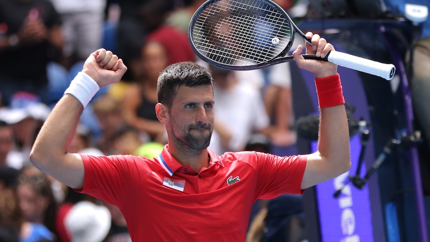 Man holds up tennis racket cheering in red shirt 
