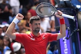 Man holds up tennis racket cheering in red shirt 