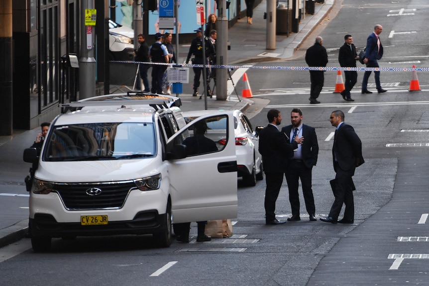 police detectives stand on an empty street with a police van