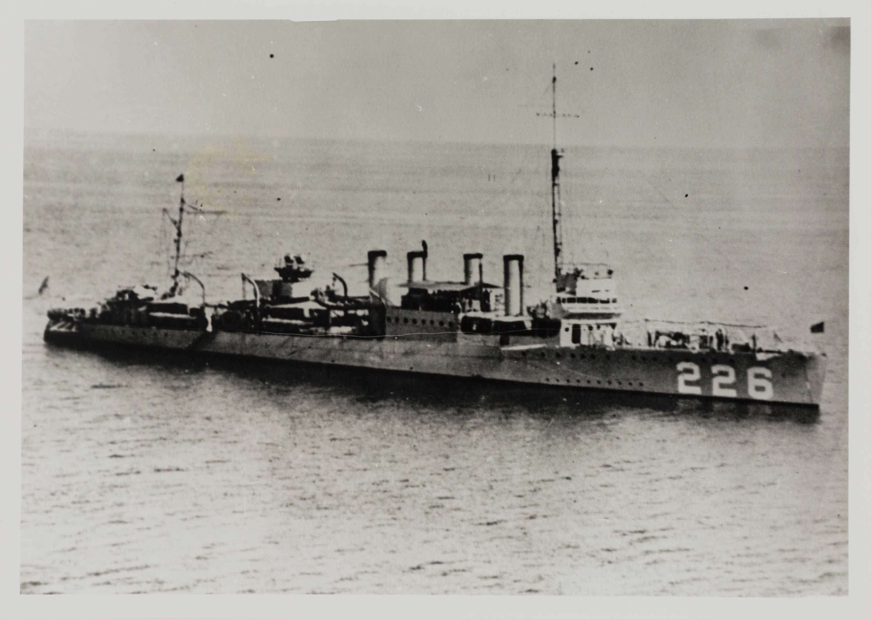 Black and white of an early 20th century warship. Four funnels, two masts, calm day