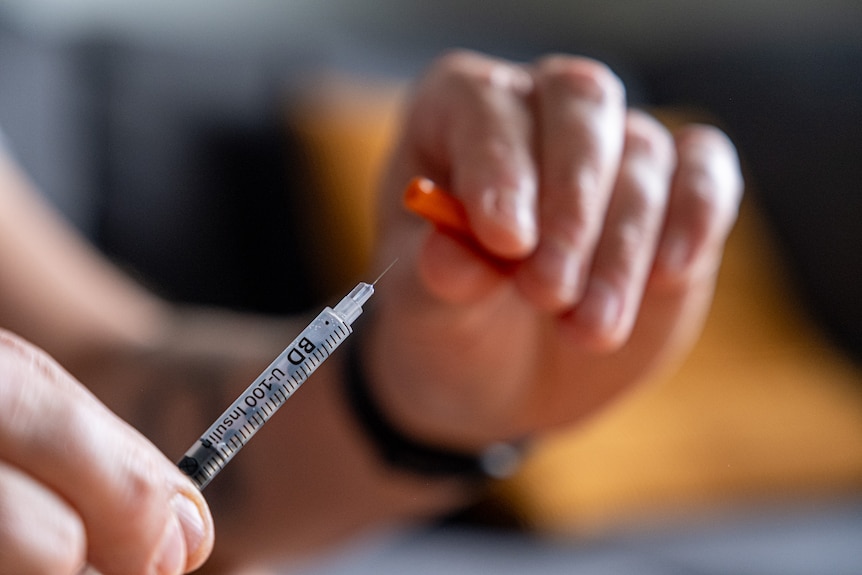 A close up of a hand pulling the cap off a syringe.