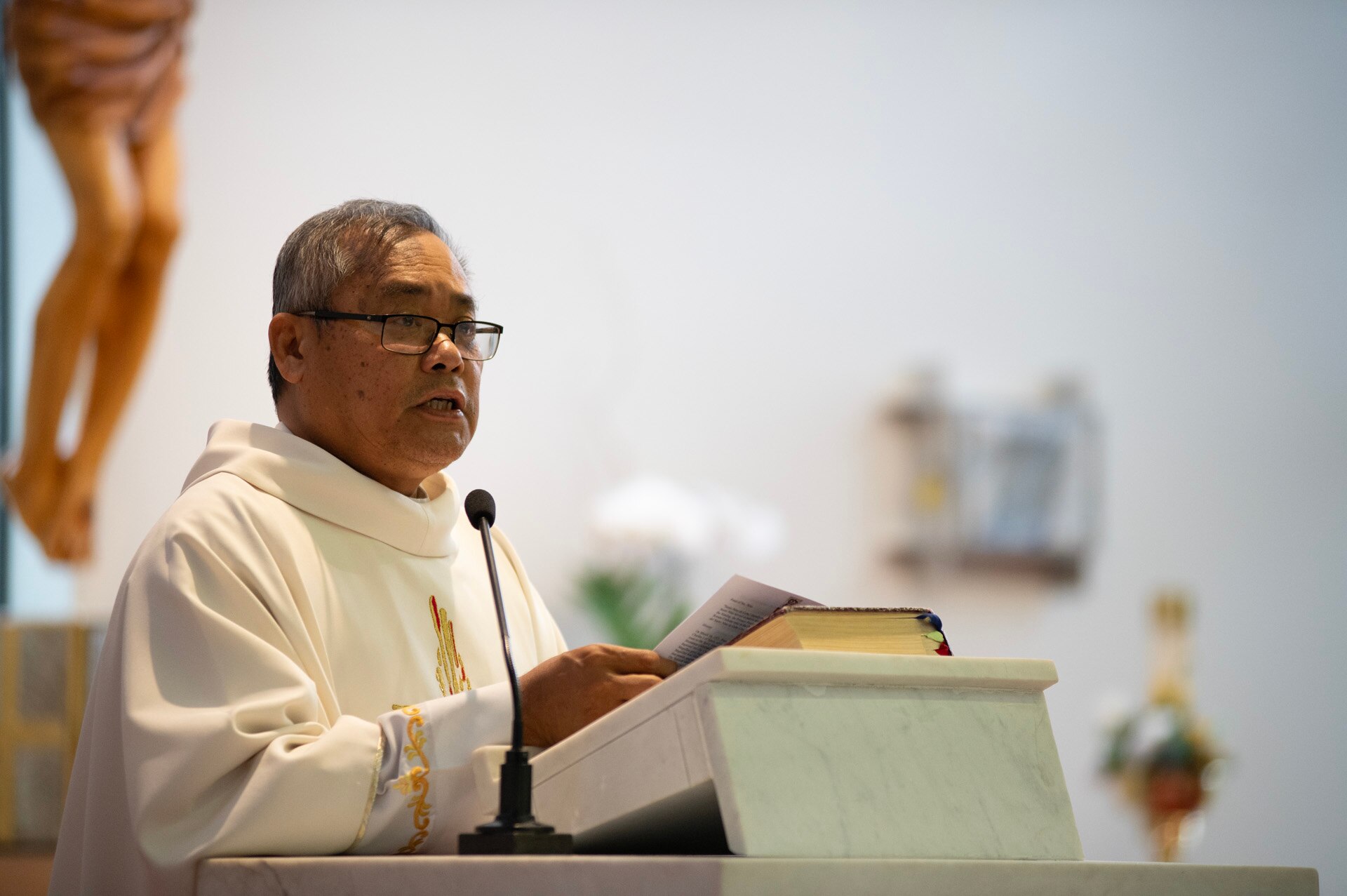 Monsignor Asis wearing white robe inside church at lecturn.
