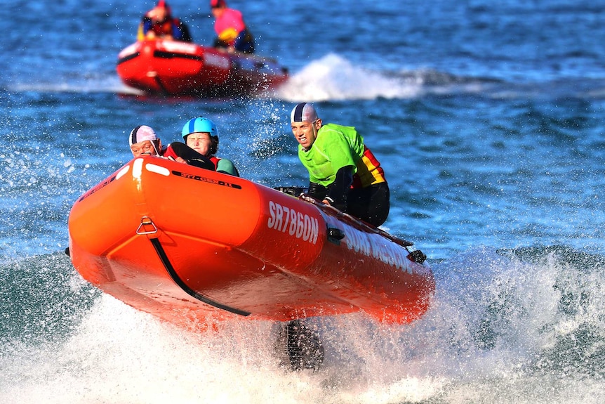 Three people ride in front of a wave in an inflatable rescue boat.