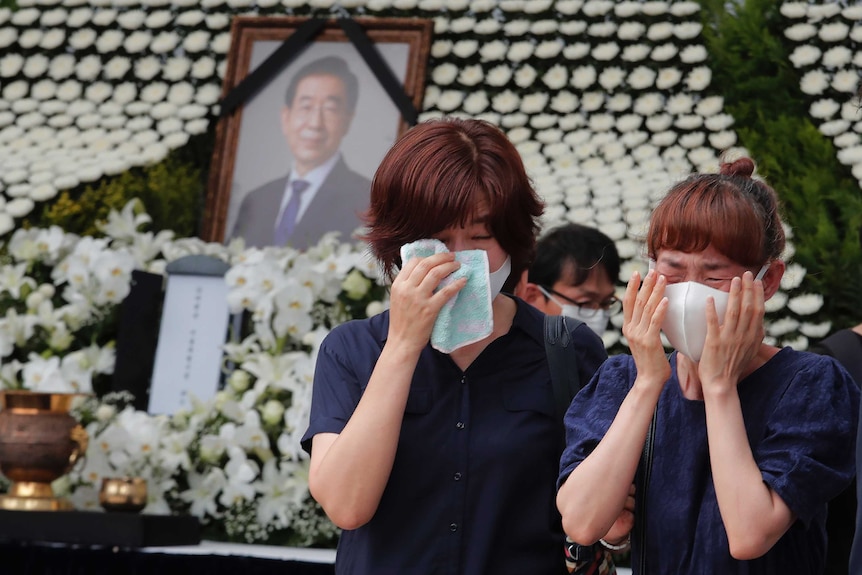 Two women in face masks weep in front of a memorial