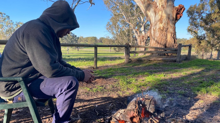 Man wearing a hoddie sitting in front of a fire.