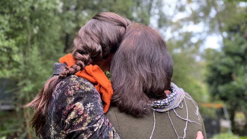 An adult daughter and her mother embrace, photo from behind
