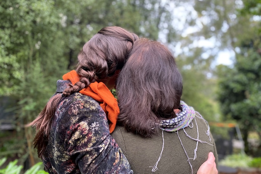 An adult daughter and her mother embrace, photo from behind