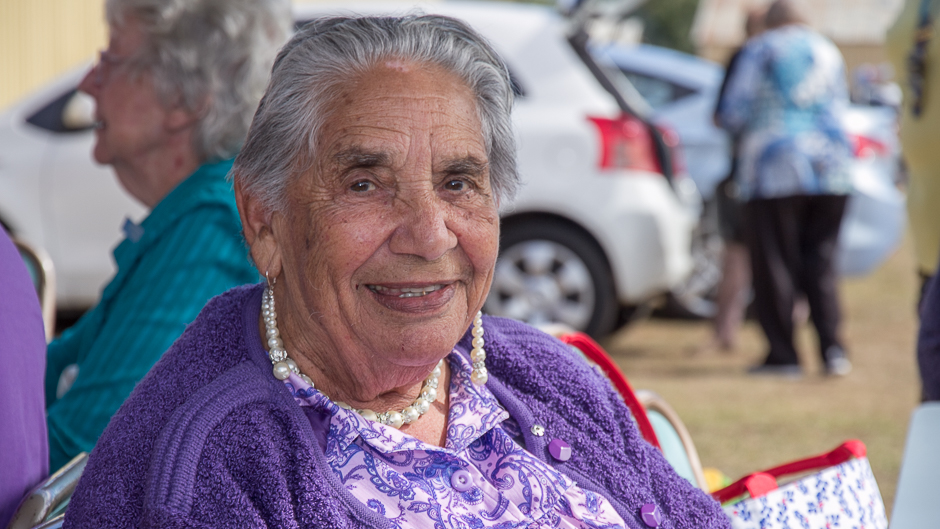 A close up of an aboriginal woman in a purple cardigan and pearls