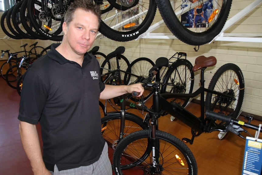 A man stands in a bike shop with his hand on the handlebars of a bike.