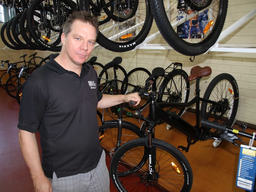 A man stands in a bike shop with his hand on the handlebars of a bike.