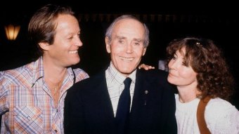 Peter Fonda puts his hand on his father Henry's shoulder and smiles at him. On Henry Fonda's other side is Shirlee Fonda.