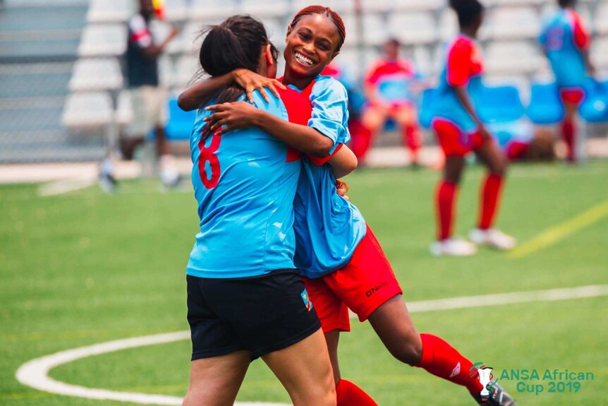 One smiling player hugs her teammate in celebration during a women's football exhibition game.