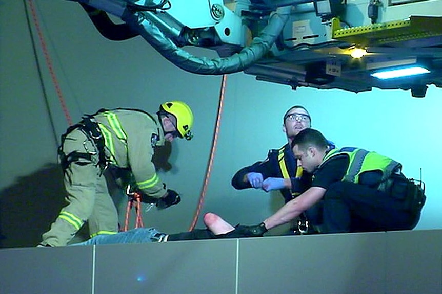 View from the street of a man lying on a ledge, his arm visible, while emergency services officers tend to him.